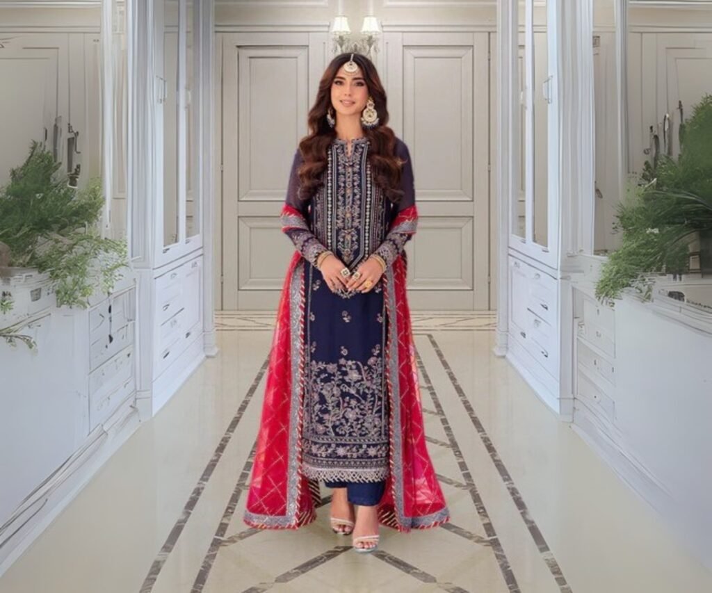 Model wearing a navy blue embroidered kurta paired with a red dupatta, standing in an elegant indoor setting